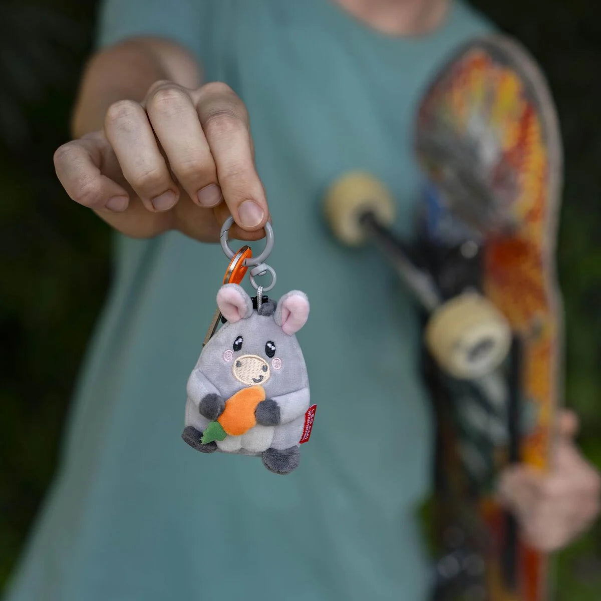 Person holding a keychain shaped like a cartoon animal with a carrot, with a skateboard in the background.